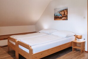 A single wooden bed with white bedding in a room with wooden flooring and a sloped ceiling.