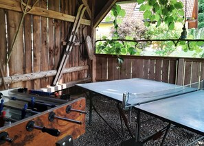 A wooden room with a table tennis table, a wooden bench, and a window with a view of trees and a building.