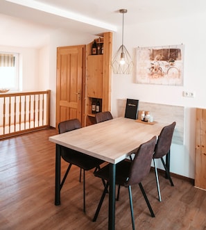 A dining area with a wooden table and chairs, a pendant light, and a wooden cabinet with bottles.