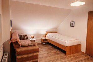 A small, cozy bedroom with a single bed, a wooden nightstand, a bedside table, and a chair.