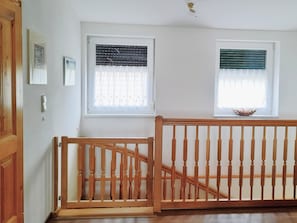 A room with two windows, a wooden railing, and a door.