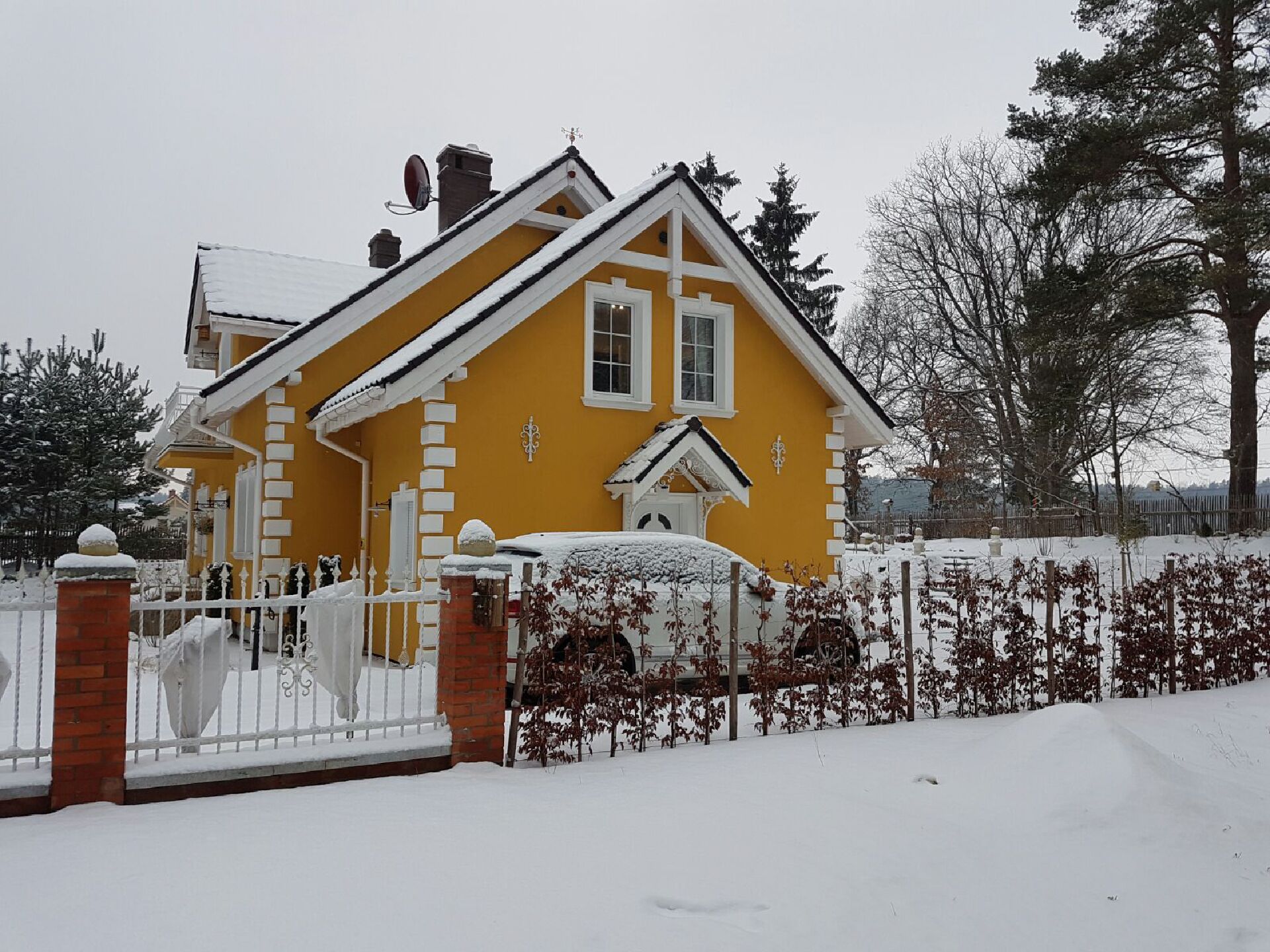 Een geel huis met een witte omheining en sneeuw op de grond.