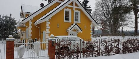 Een geel huis met een witte omheining en sneeuw op de grond.