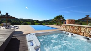 Un jacuzzi con pared de piedra, terraza de madera y piscina.