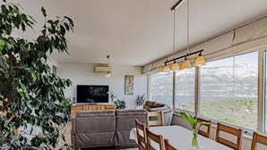 Una sala de estar moderna con un televisor grande, asientos cómodos, un comedor y vistas a un lago y montañas.