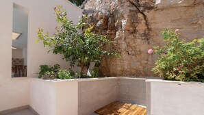 Un pequeño espacio exterior con ducha, piso de madera, rodeado de plantas y una pared de piedra.