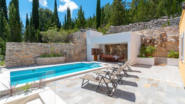 Un área de piscina moderna al aire libre con paredes de piedra, sillones reclinables y un comedor.