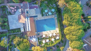 Eine Vogelperspektive eines Resorts mit einem zentralen Schwimmbecken, mehreren Liegebereichen und umgebender Vegetation.