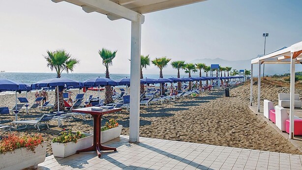 Eine Terrasse direkt am Strand mit Liegestühlen, Sonnenschirmen und Kübelpflanzen.