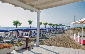 Een terras aan het strand met ligbedden, parasols en plantenpotten.
