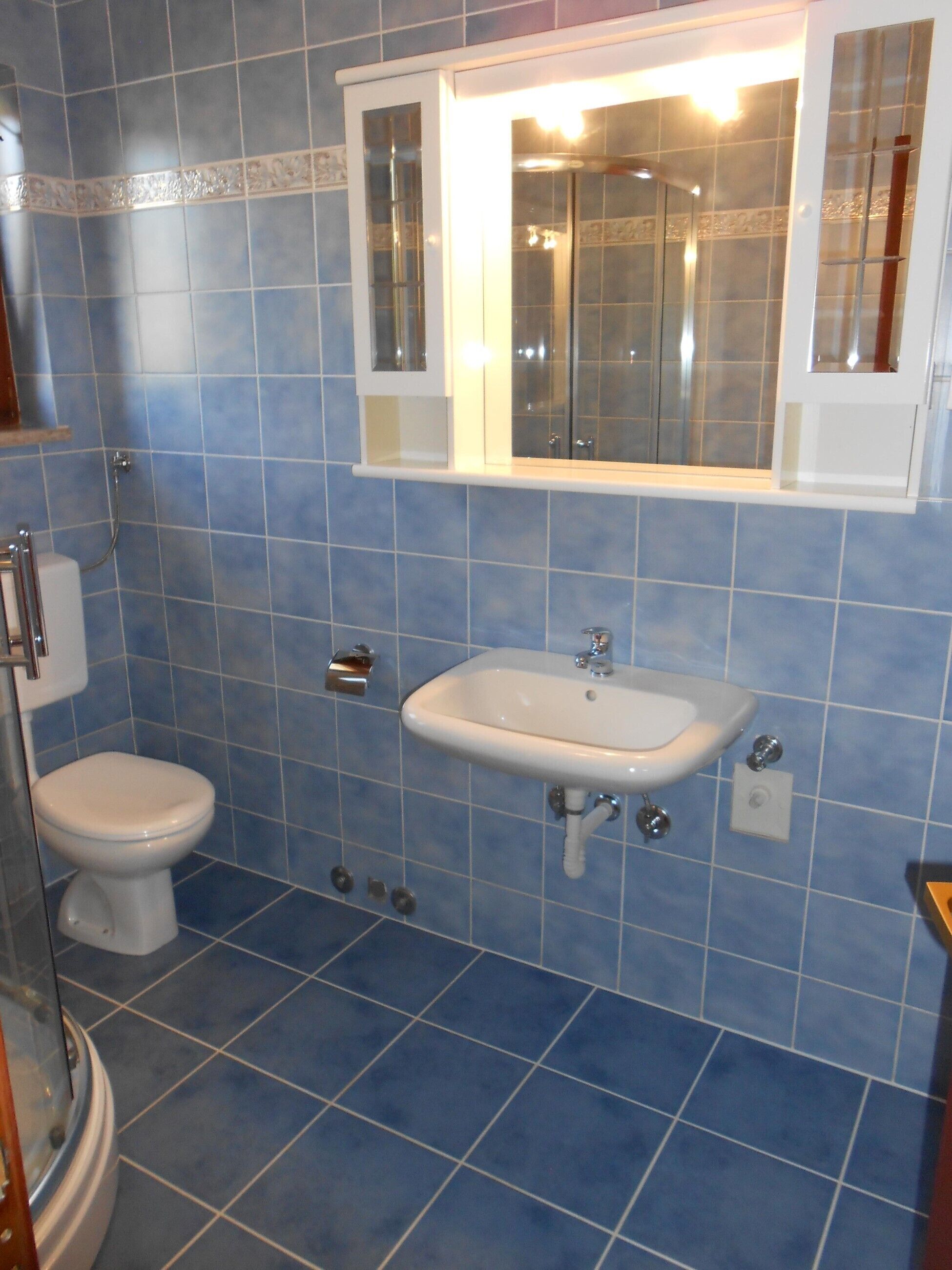 A bathroom with blue tiles, a white sink, and a toilet.