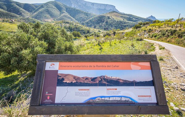 Un panneau indicateur présentant un paysage pittoresque de montagnes et d’une route, et indiquant le tracé d’un sentier de randonnée.