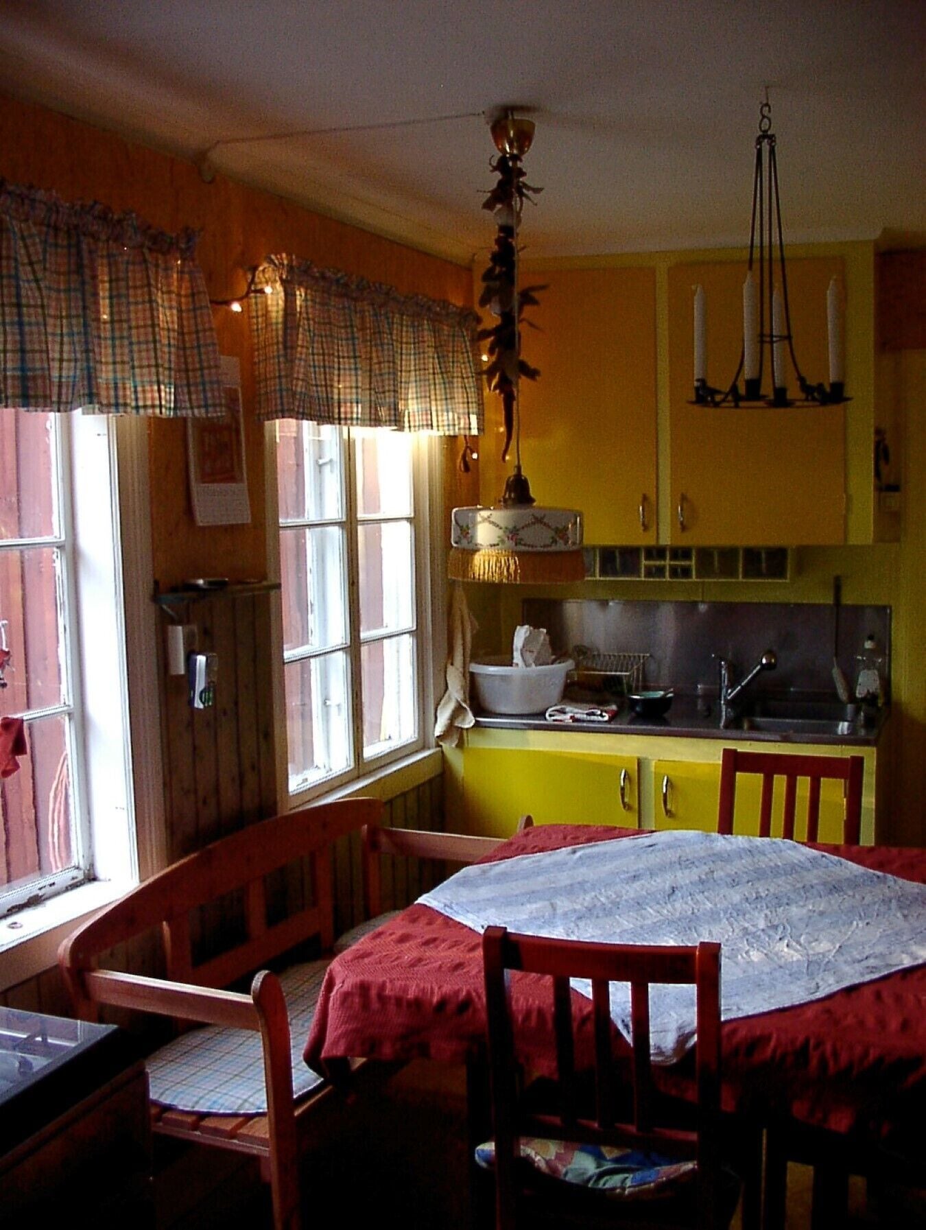 A kitchen with yellow cabinets, a dining table with a red tablecloth, and a hanging light fixture.