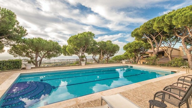En swimmingpool med kristallklart blått vatten, omgiven av träd och med utsikt över havet.