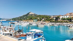 Una marina con barche ormeggiate, una collina con edifici sullo sfondo e cielo azzurro.