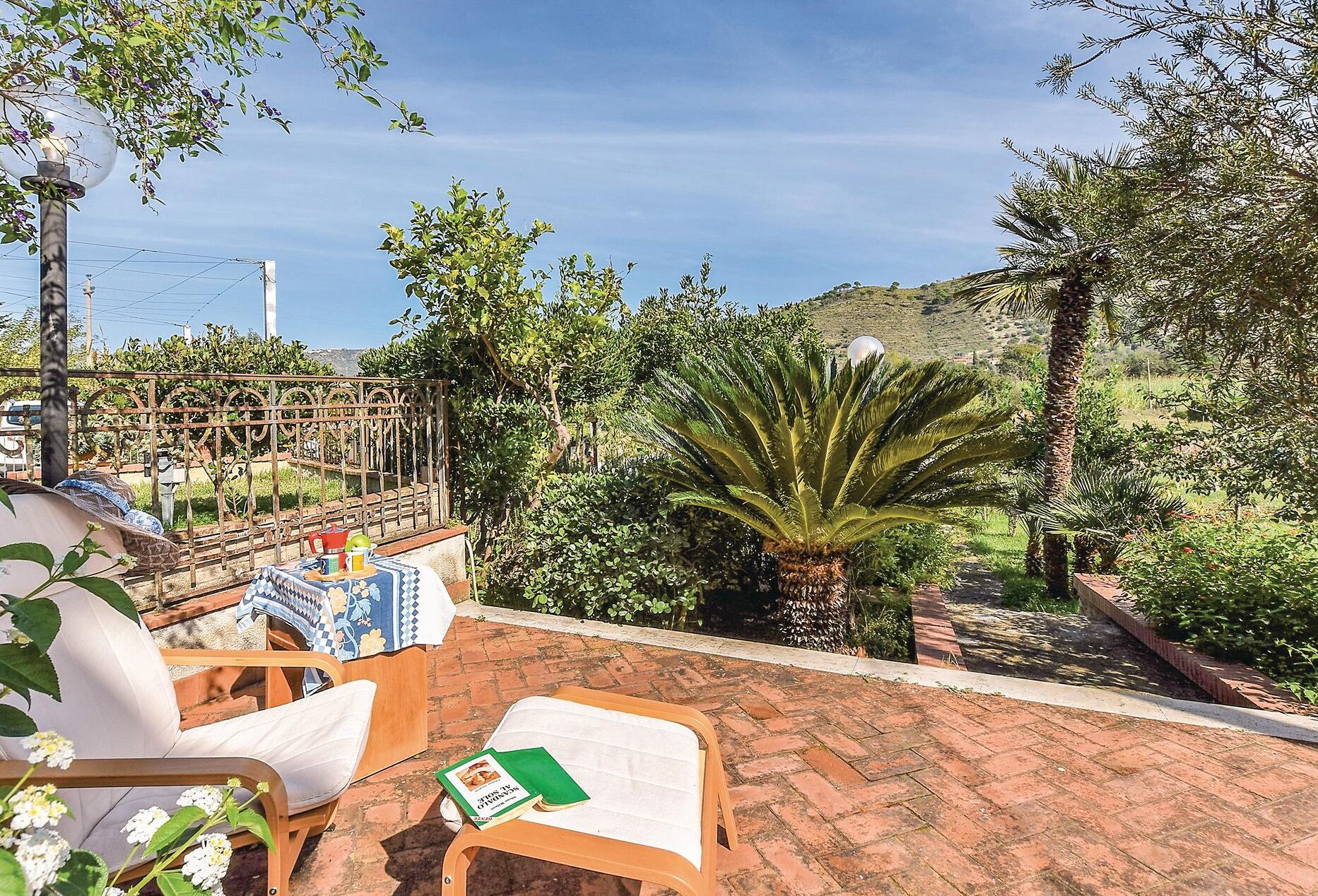 A patio with two lounge chairs, a table with a patterned tablecloth, and a book.