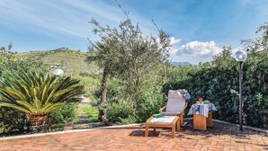 Un patio con una sedia e un tavolo, immerso nel verde e sotto un cielo sereno.