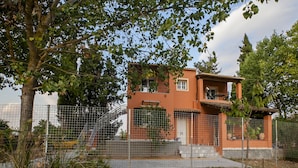 Un edificio a due piani con facciata rossa, un balcone al piano superiore e un'area recintata in primo piano.