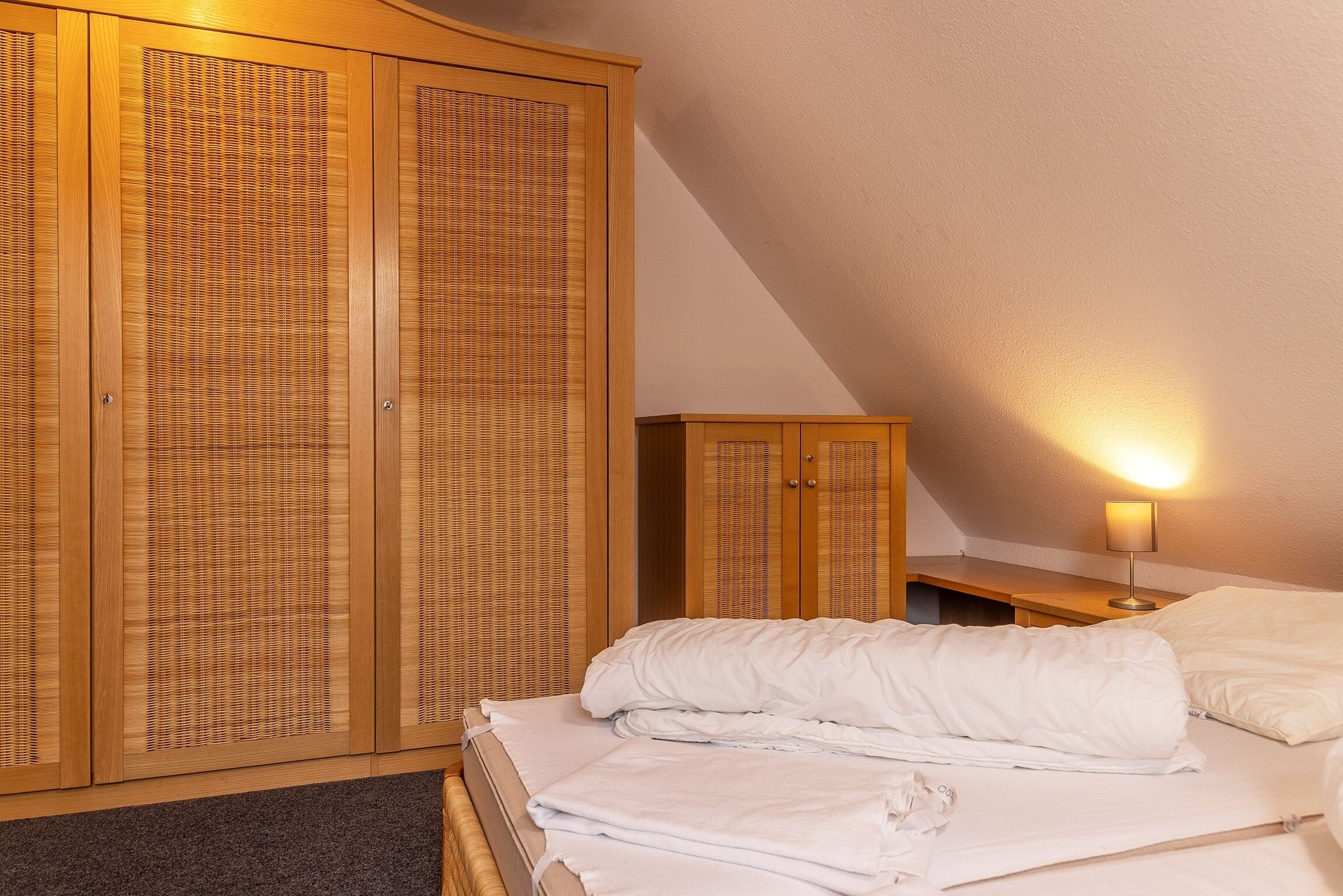 A bedroom with a bed, a wooden wardrobe, and a bedside table with a lamp.