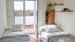 A room with two beds, a sliding glass door leading to a balcony, and a wooden shelf with decorative items. - Beach front apartment in Cartagena (Cartagena)