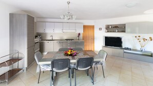 Una cucina moderna con zona pranzo, che include un tavolo con sedie, un televisore e un vaso con fiori.