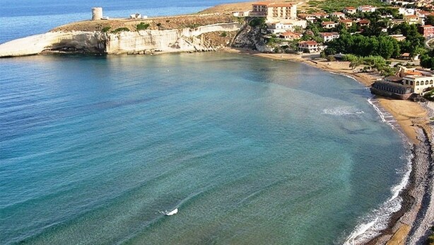 Una località costiera con spiaggia limpida, un'imponente struttura fortificata e edifici residenziali.