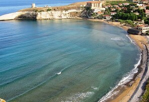 A coastal town with a clear beach, a fortified structure, and residential buildings.