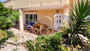 Un edificio con un patio che presenta un tavolo e sedie di legno, circondato da diverse piante e cactus.