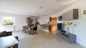 Una cucina moderna con zona pranzo, TV e un vaso con fiori secchi su un tavolo consolle.