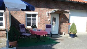 A brick building with a red-tiled roof, a white door, and a small porch area with a table and chairs. - Holiday house, Martha``am Szczecin Lagoon / Meck / Pom / Ueckermünde-Bellin (Ueckermünde)