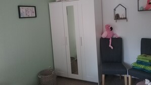 A room with a white wardrobe, a framed picture on the wall, a pink flamingo decoration, and a chair with a stack of folded blankets. - Holiday house, Martha``am Szczecin Lagoon / Meck / Pom / Ueckermünde-Bellin (Ueckermünde)