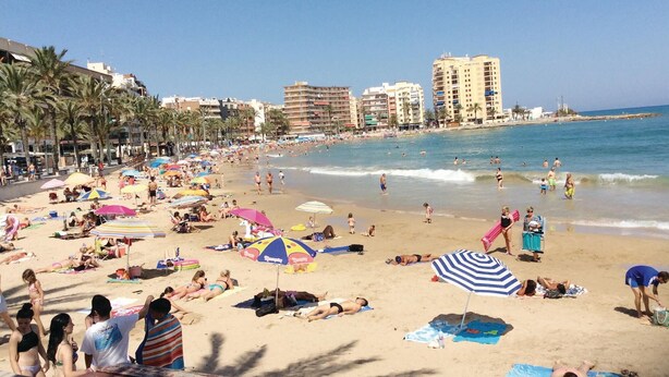 Una playa concurrida, llena de sombrillas y gente tomando el sol.
