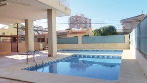 Una piscina con borde de azulejos, una escalera metálica y un suelo de hormigón.