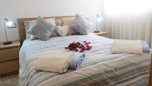 Una cama bien hecha con ropa de cama a rayas, dos lámparas de noche y una rosa en la cama.