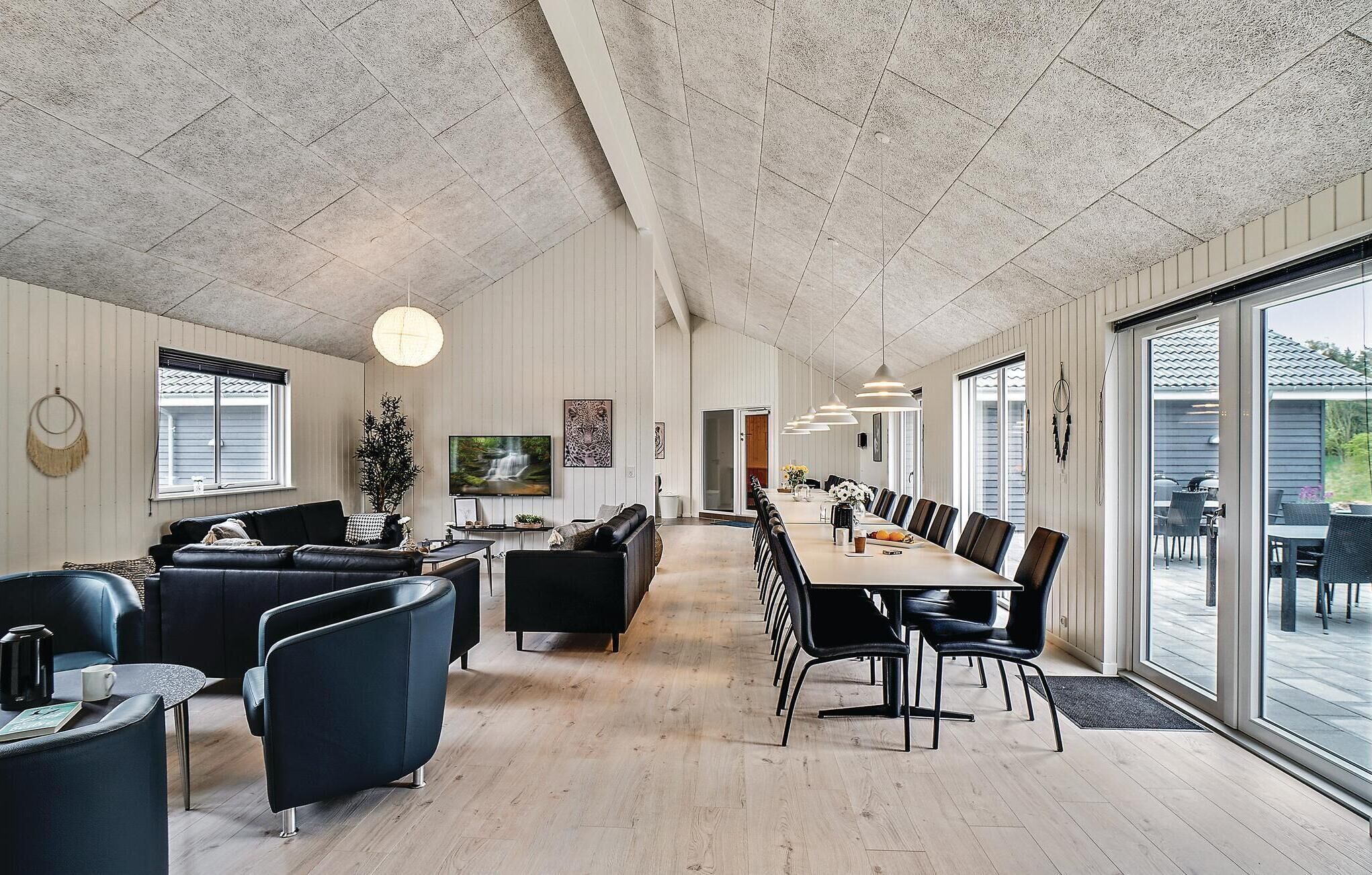 A spacious living area with a long dining table, black leather sofas, and a large TV.