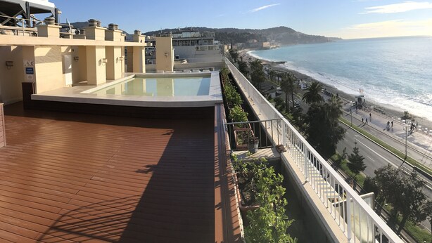 Una terraza con piscina, vista a la playa y un paisaje urbano al fondo.