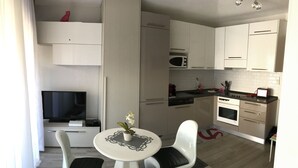 Cocina compacta con armarios blancos, microondas y un pequeño comedor con mesa y sillas.