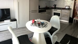 Una cocina moderna con armarios blancos, microondas y cafetera. Hay una mesa de comedor con dos sillas y un televisor pequeño sobre un mueble.