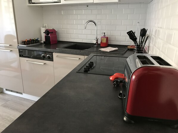 A modern kitchen with a black countertop, a red toaster, a sink, and a dishwasher.