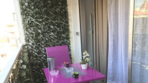 Un balcón con una mesa rosa, una planta en maceta y un recipiente metálico.