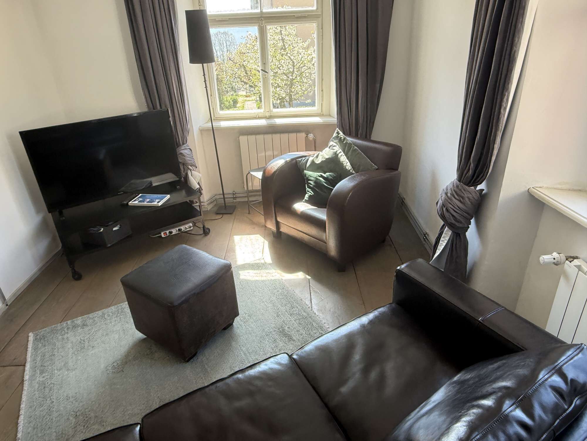 Una sala de estar con televisión de pantalla plana, un sofá, un sillón y un pequeño reposapiés.