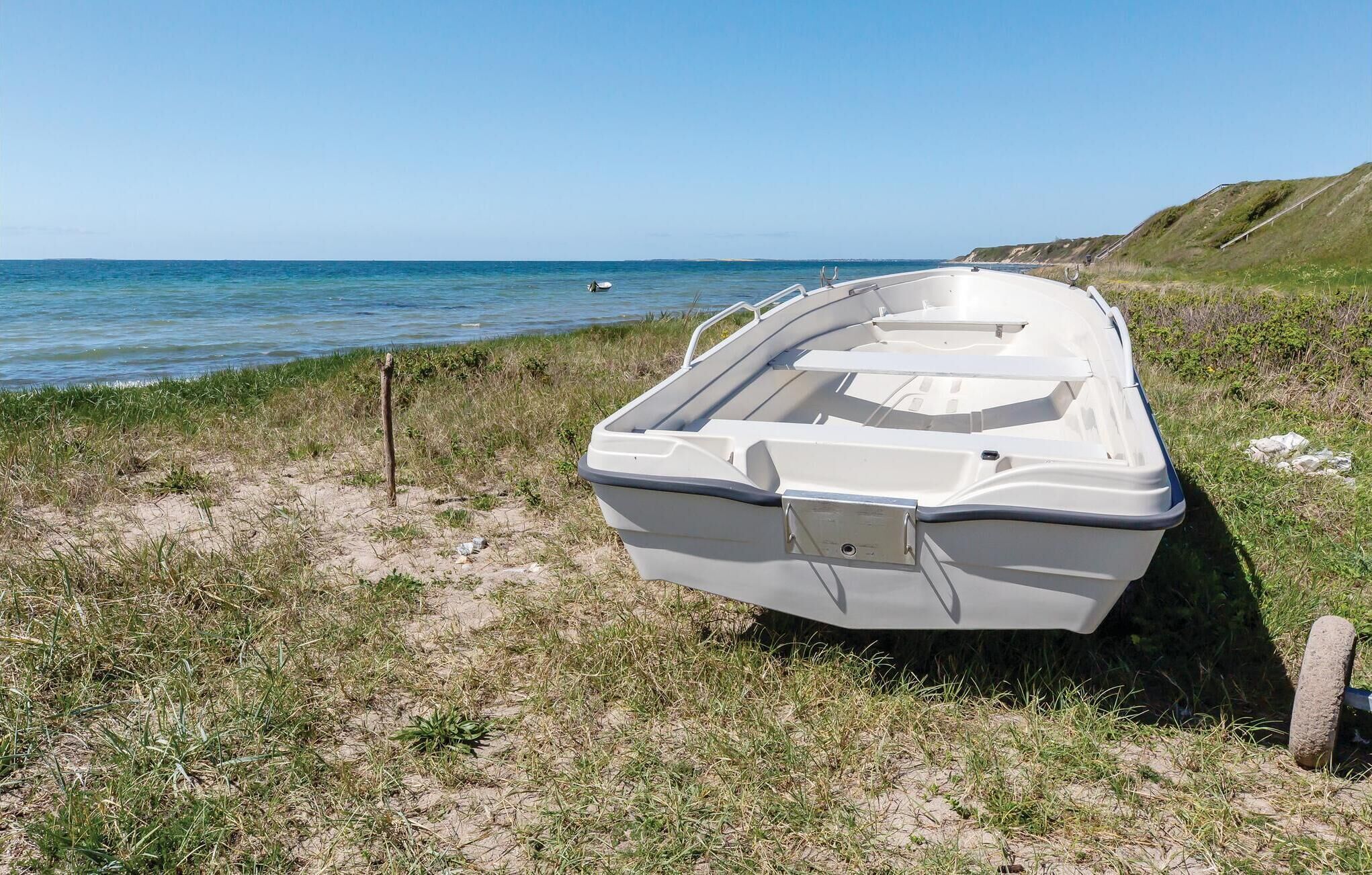 Ein weißes Boot liegt auf einem grasbewachsenen Strand mit freiem Blick auf das Meer und einen felsigen Felsen im Hintergrund.