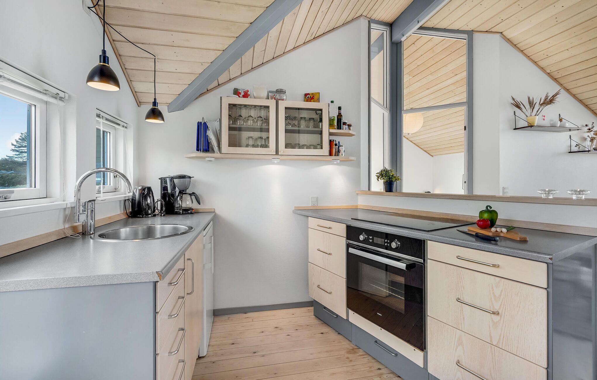 A modern kitchen with a central island, built-in oven, and a window overlooking a garden.
