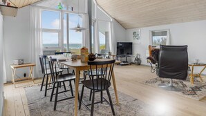 Ein geräumiger Wohnbereich mit Esstisch, Stühlen, Fernseher und Meerblick.