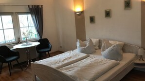 A bedroom with a double bed, a bedside table, a chair, a small round table, and a window with curtains. - small cozy apartment in a very quiet location (Prerow)