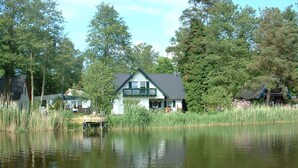 A lakeside house with a dock, surrounded by tall trees and a calm lake. - small cozy apartment in a very quiet location (Prerow)