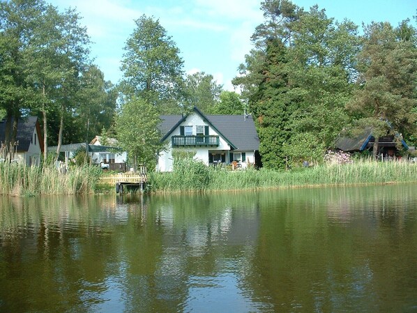 A lakeside house with a dock, surrounded by tall trees and a calm lake.