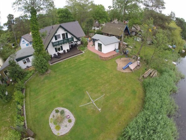 A residential area with a house featuring a fenced yard, a small garden, and a dock by the water.