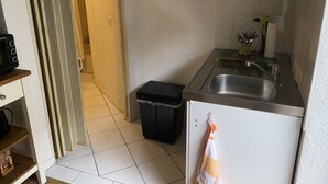 A small kitchen with a sink, a trash bin, and a refrigerator. There is a door leading to another room and a painting on the wall. - small cozy apartment in a very quiet location (Prerow)