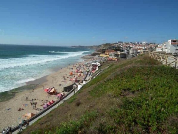 A coastal beach with a promenade, beach umbrellas, and a wooden walkway.